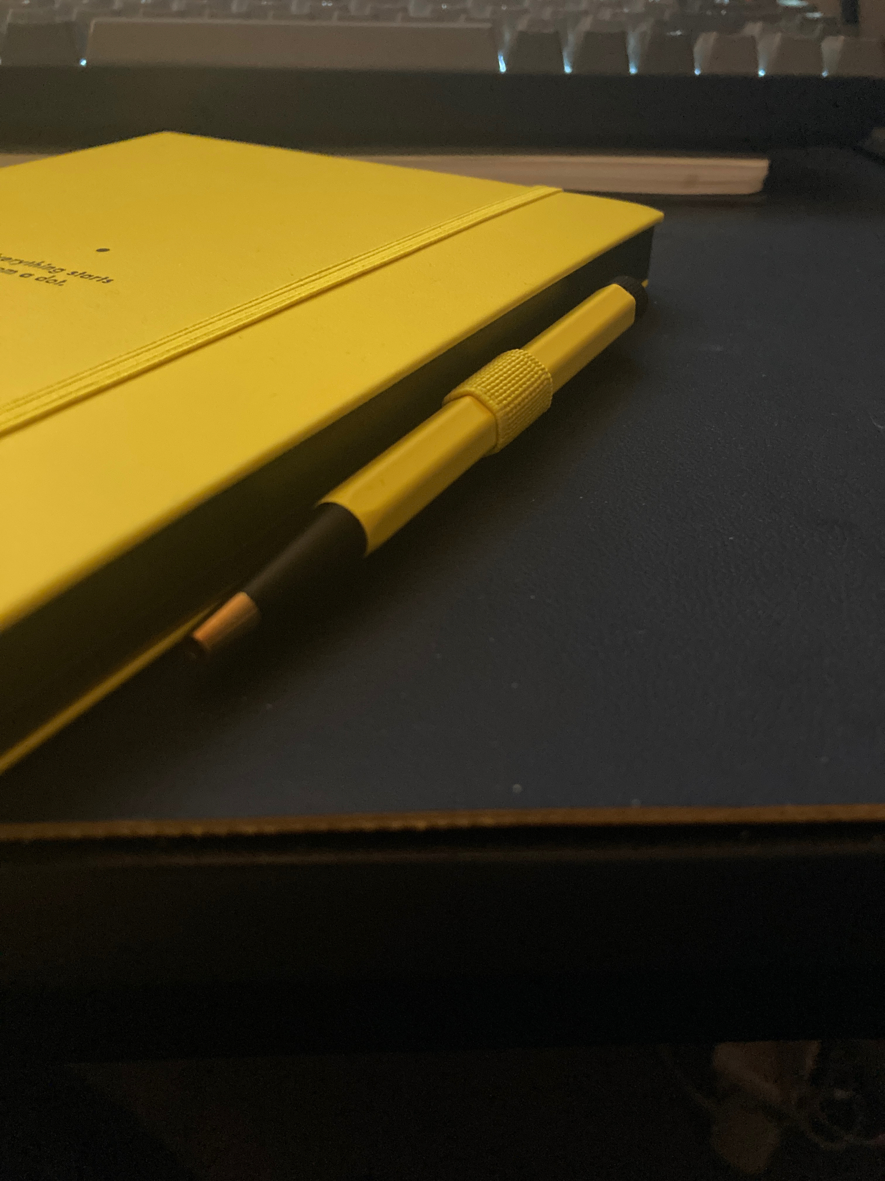 The side of a notebook, with a pen loop attached and filled with a colour-matching yellow pen.